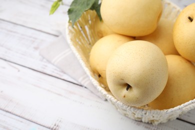 Delicious fresh apple pears in wicker basket on white wooden table, closeup. Space for text