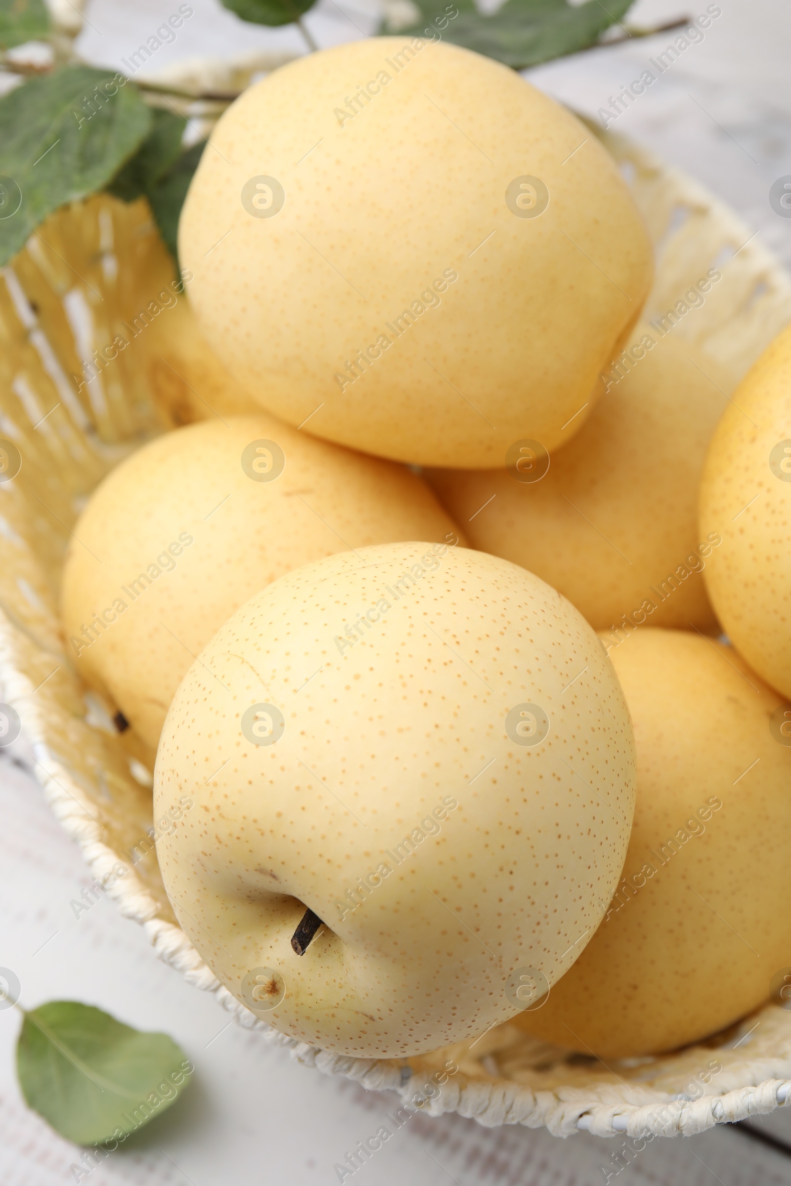 Photo of Delicious fresh apple pears in wicker basket on white table, closeup