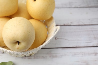 Delicious fresh apple pears in wicker basket on white wooden table, closeup. Space for text