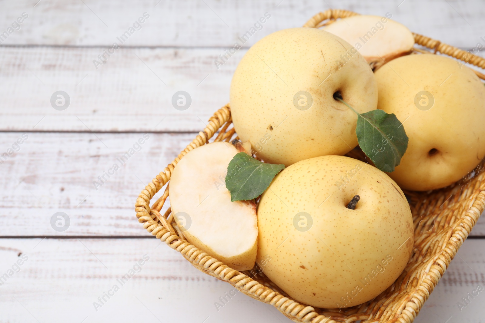 Photo of Delicious fresh apple pears in wicker basket on white wooden table, closeup