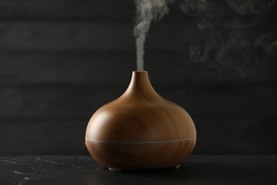 Photo of Aroma oil diffuser with steam on black table