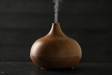 Photo of Aroma oil diffuser with steam on black table