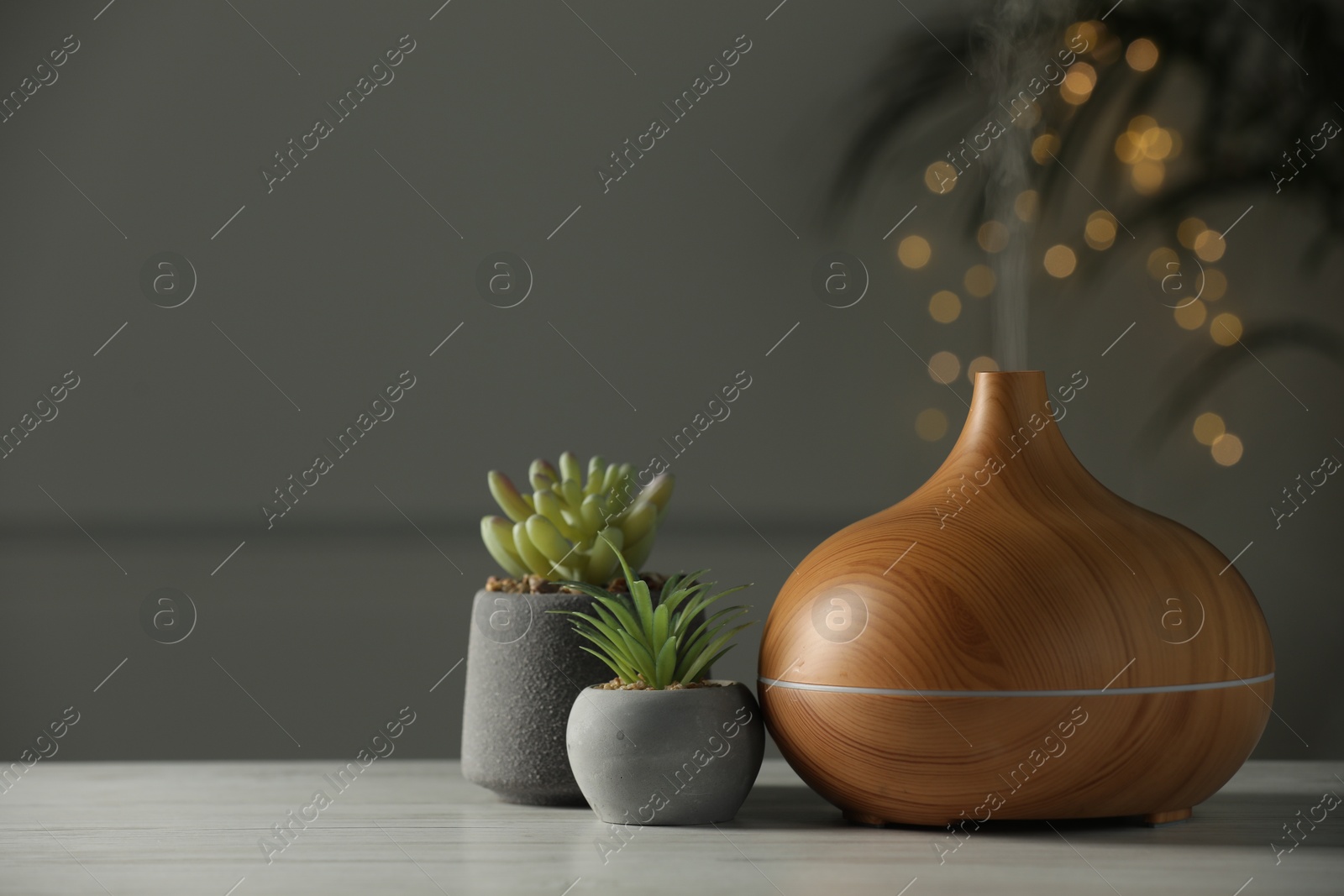 Photo of Aroma oil diffuser and houseplants on white wooden table, space for text