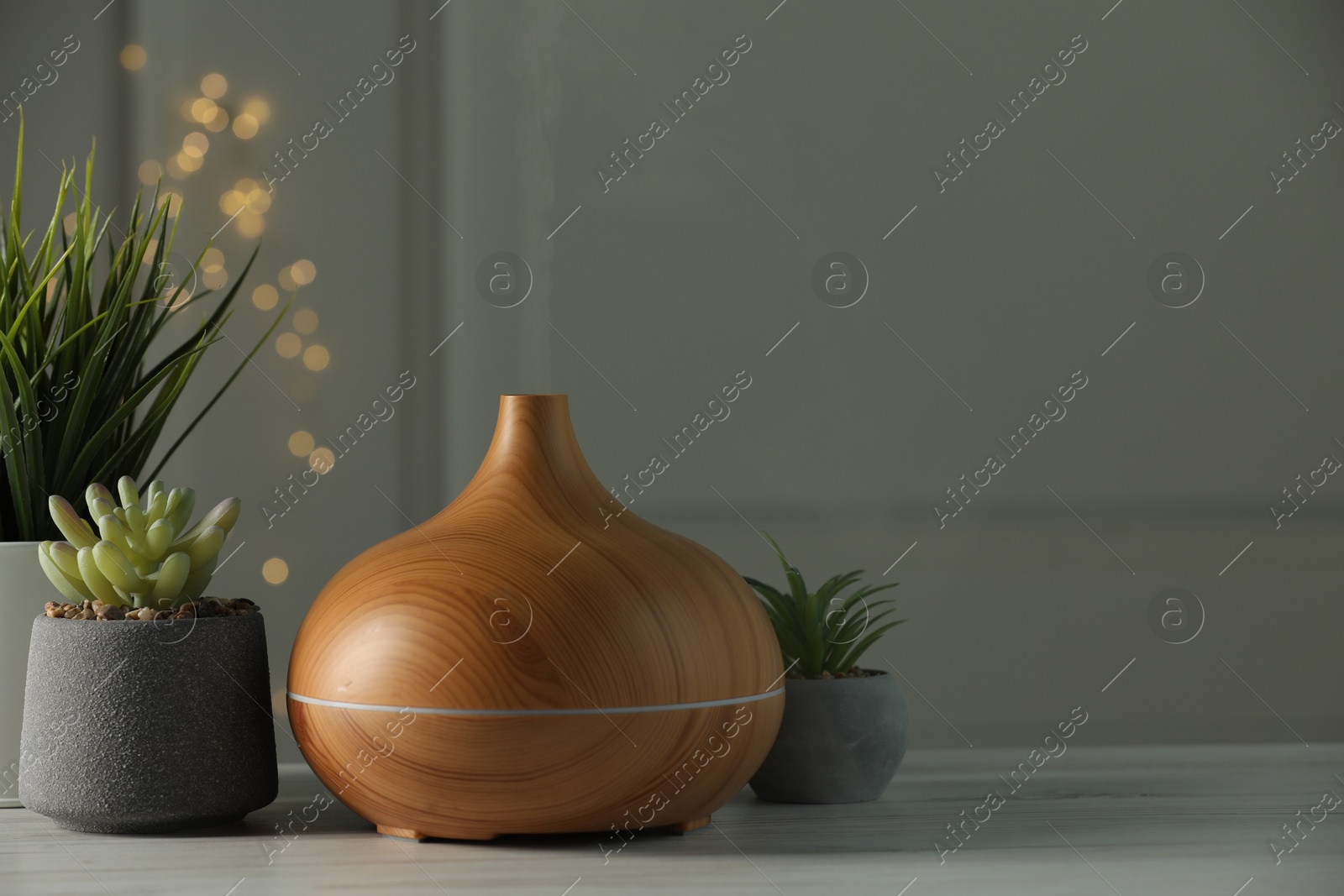 Photo of Aroma oil diffuser and houseplants on white wooden table, space for text