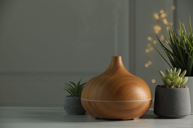 Photo of Aroma oil diffuser and houseplants on white wooden table, space for text