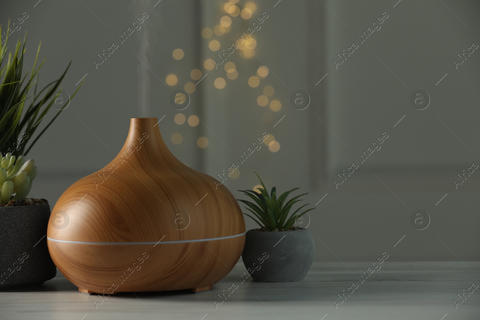 Photo of Aroma oil diffuser and houseplants on white wooden table, space for text