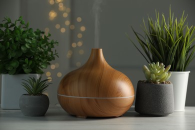 Aroma oil diffuser and houseplants on white wooden table