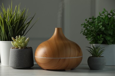 Aroma oil diffuser and houseplants on white wooden table