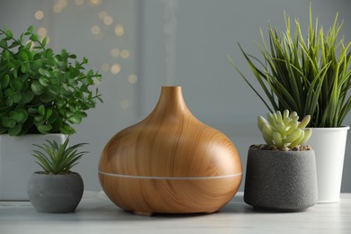 Aroma oil diffuser and houseplants on white wooden table