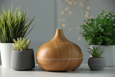 Aroma oil diffuser and houseplants on white wooden table