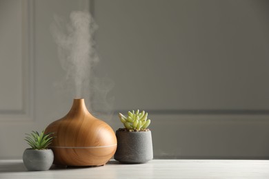 Photo of Aroma oil diffuser and houseplants on white wooden table, space for text