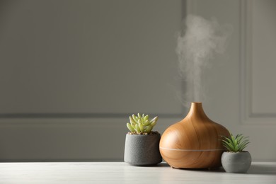 Aroma oil diffuser and houseplants on white wooden table, space for text