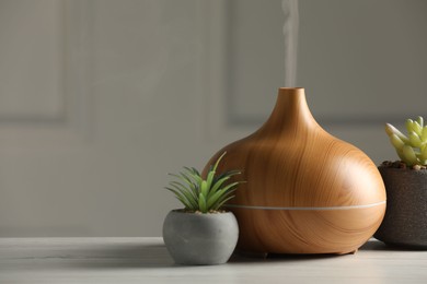 Photo of Aroma oil diffuser and houseplants on white wooden table, space for text