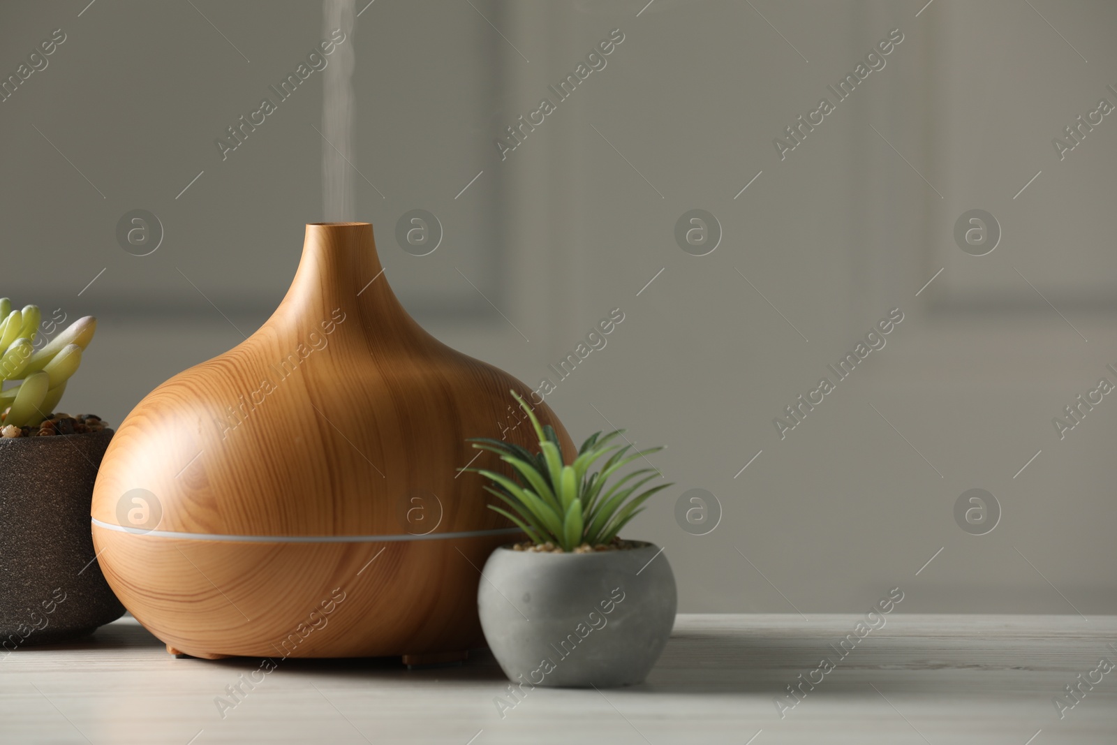 Photo of Aroma oil diffuser and houseplants on white wooden table, space for text