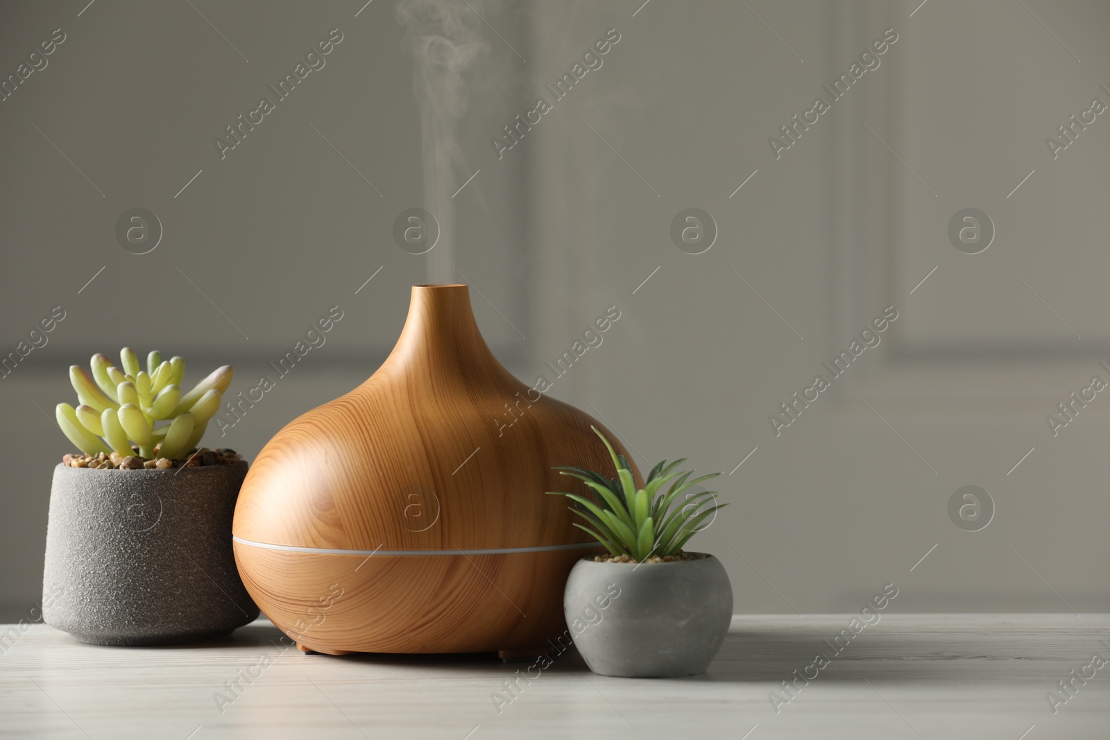 Photo of Aroma oil diffuser and houseplants on white wooden table, space for text