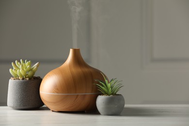 Photo of Aroma oil diffuser and houseplants on white wooden table, space for text