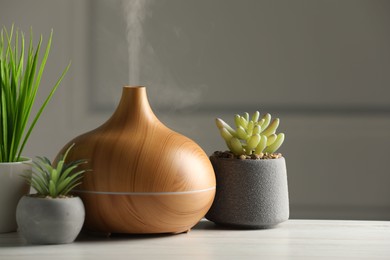 Photo of Aroma oil diffuser and houseplants on white wooden table