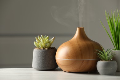 Photo of Aroma oil diffuser and houseplants on white wooden table