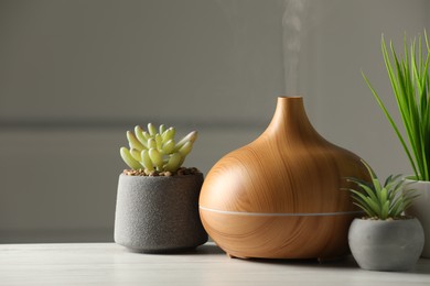 Aroma oil diffuser and houseplants on white wooden table