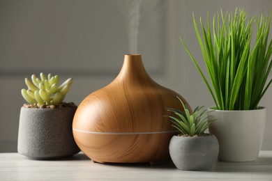 Photo of Aroma oil diffuser and houseplants on white wooden table