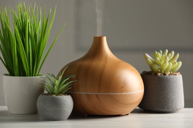 Photo of Aroma oil diffuser and houseplants on white wooden table