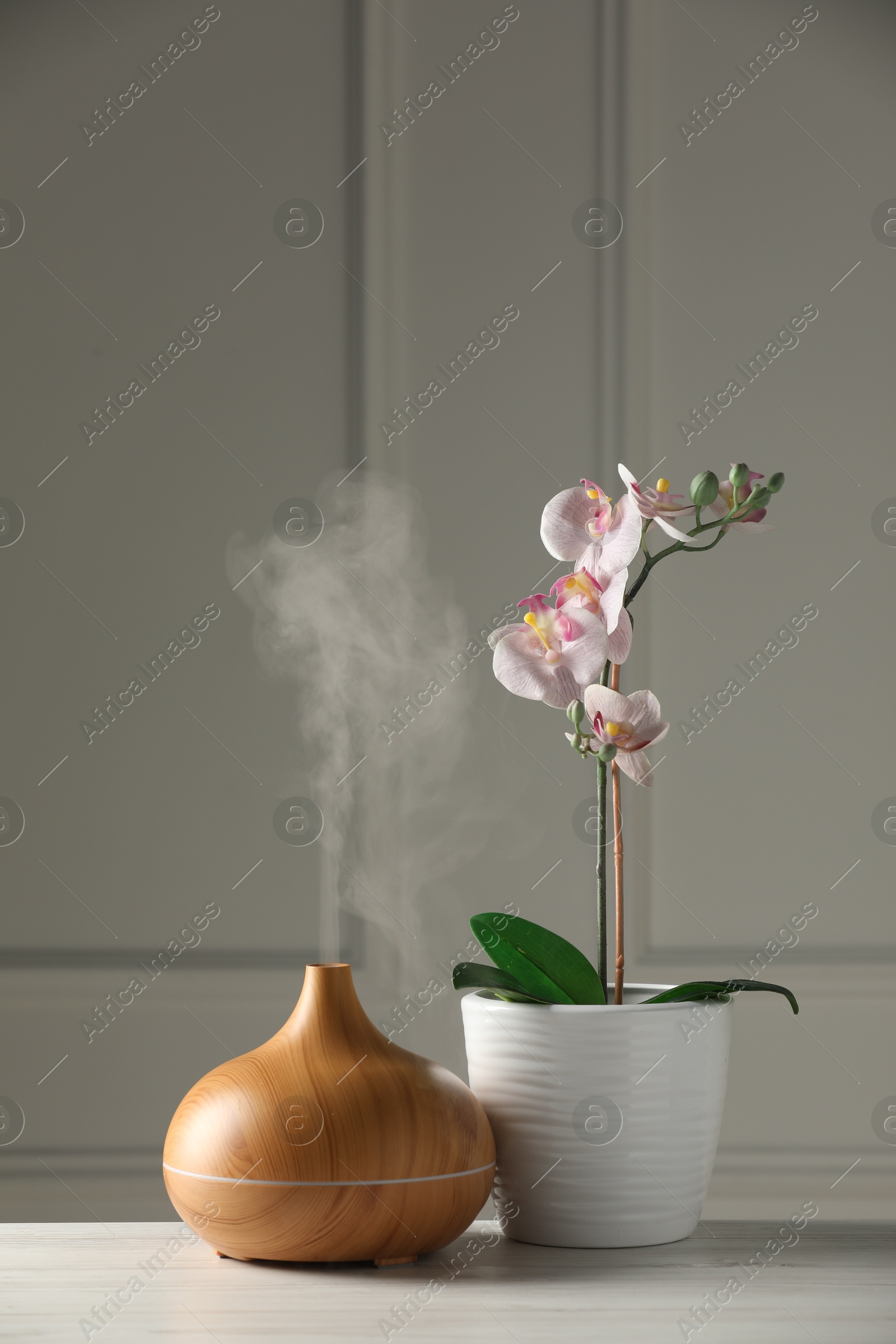 Photo of Aroma oil diffuser and orchid flower on white wooden table