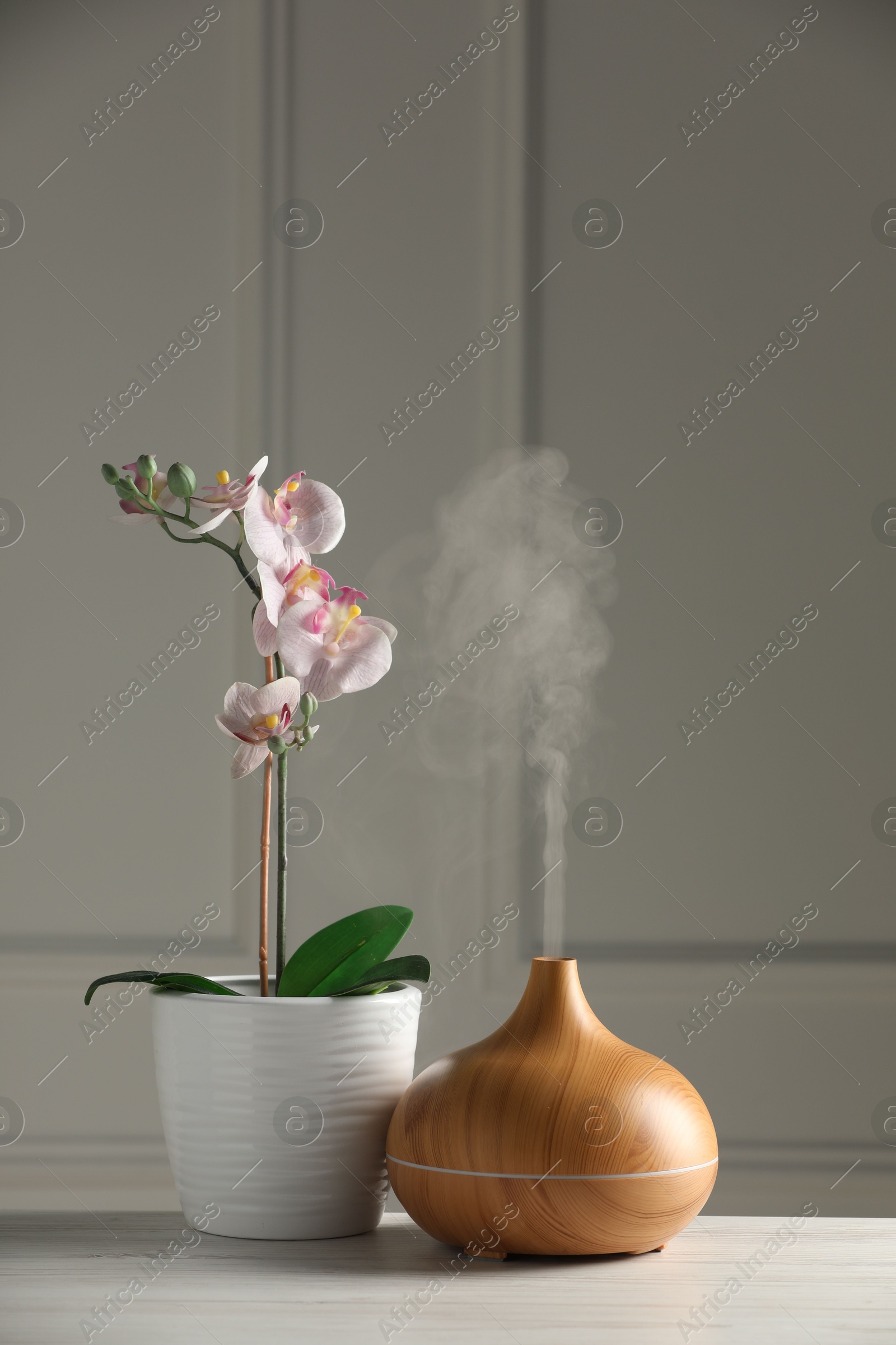 Photo of Aroma oil diffuser and orchid flower on white wooden table