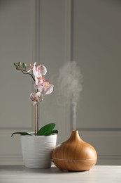 Aroma oil diffuser and orchid flower on white wooden table