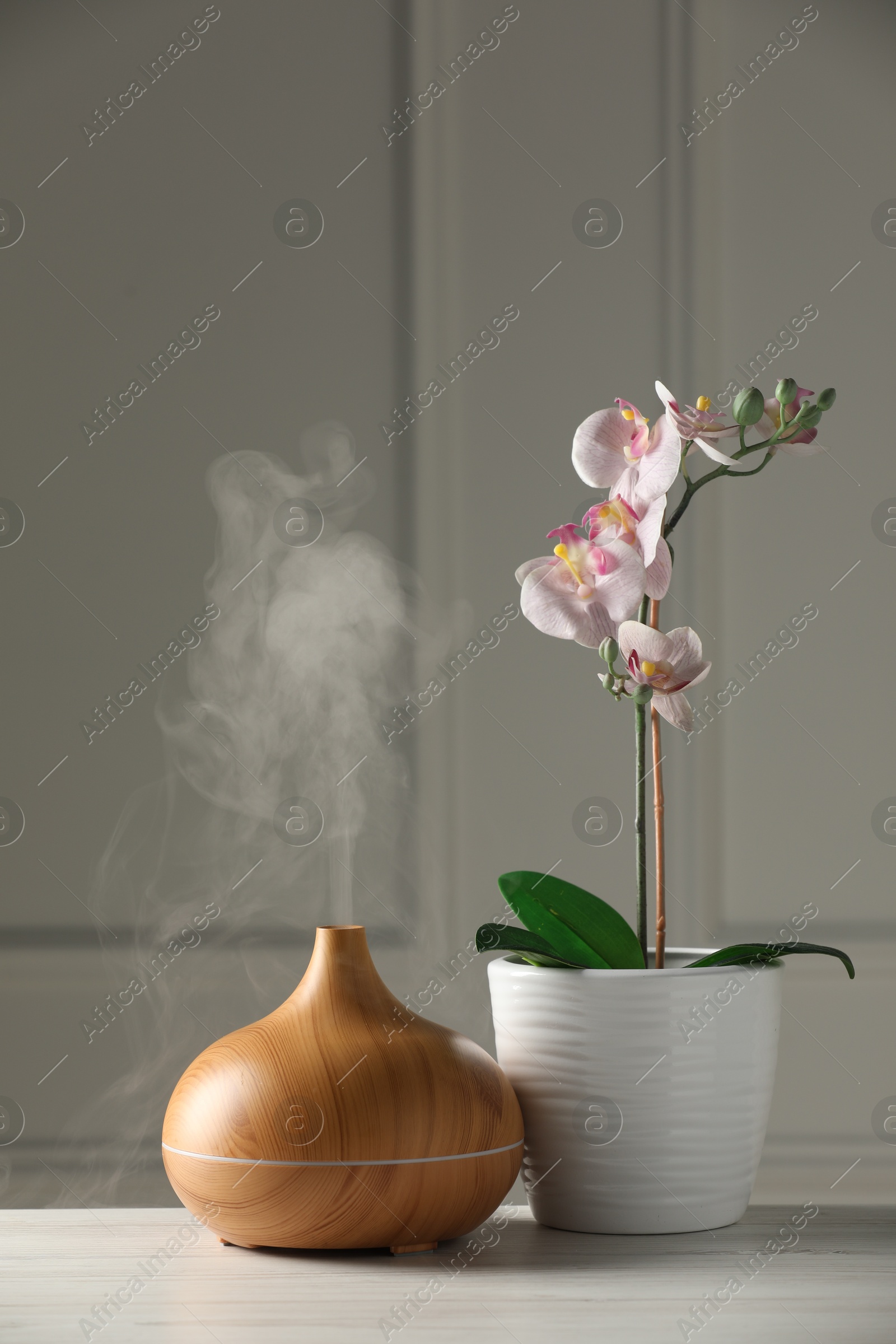 Photo of Aroma oil diffuser and orchid flower on white wooden table