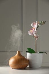 Aroma oil diffuser and orchid flower on white wooden table