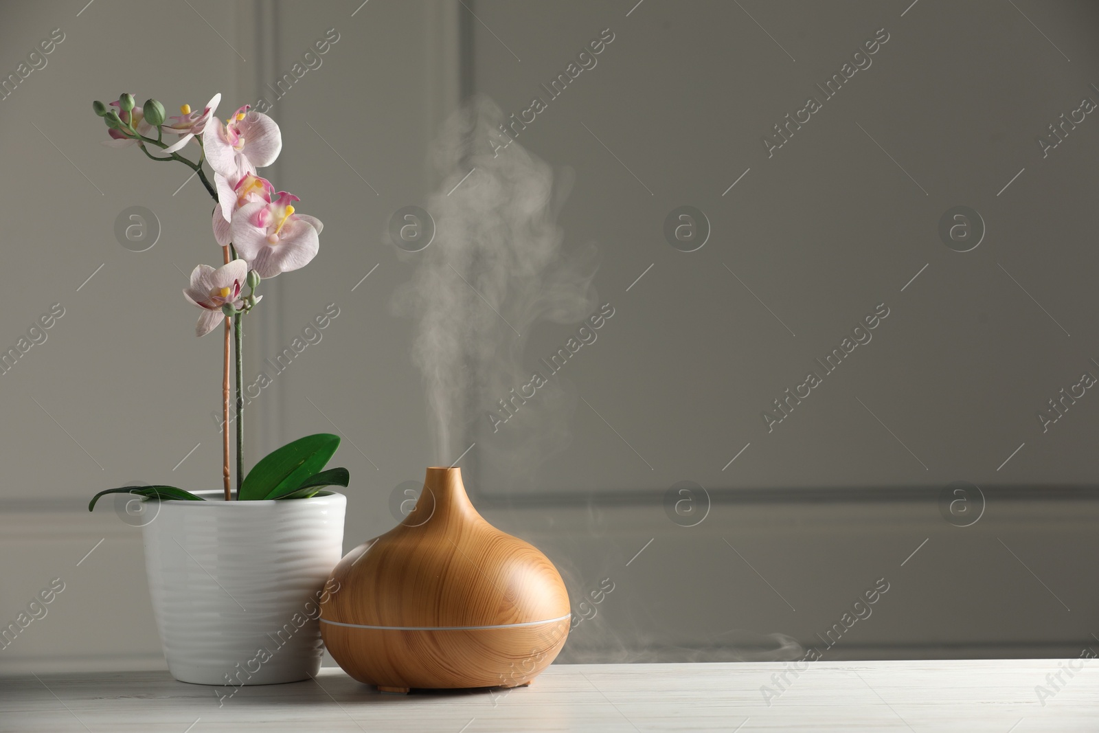 Photo of Aroma oil diffuser and orchid flower on white wooden table, space for text