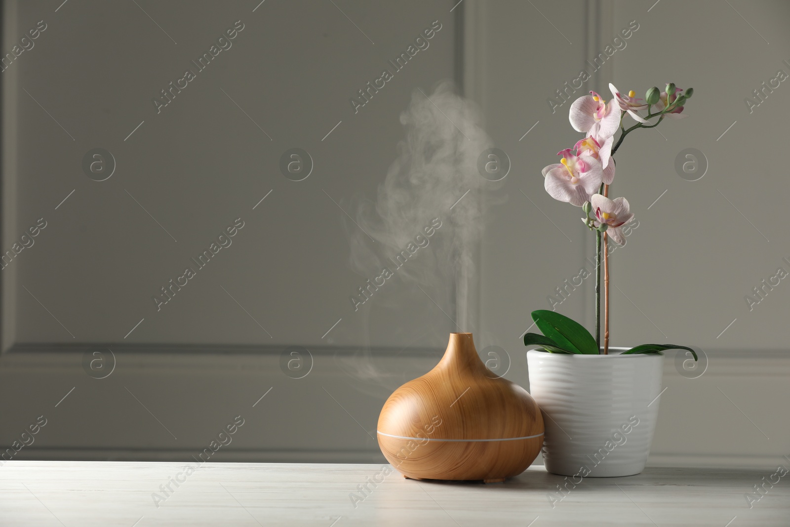 Photo of Aroma oil diffuser and orchid flower on white wooden table, space for text