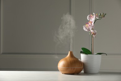 Photo of Aroma oil diffuser and orchid flower on white wooden table, space for text