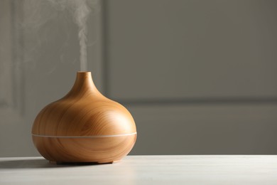 Aroma oil diffuser on white wooden table, space for text