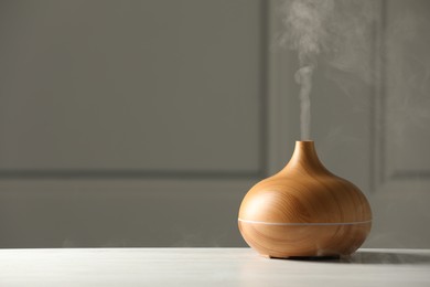 Aroma oil diffuser on white wooden table, space for text