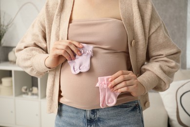 Expecting twins. Pregnant woman holding two pairs of socks at home, closeup