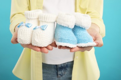 Expecting twins. Pregnant woman holding two pairs of baby shoes on light blue background, closeup