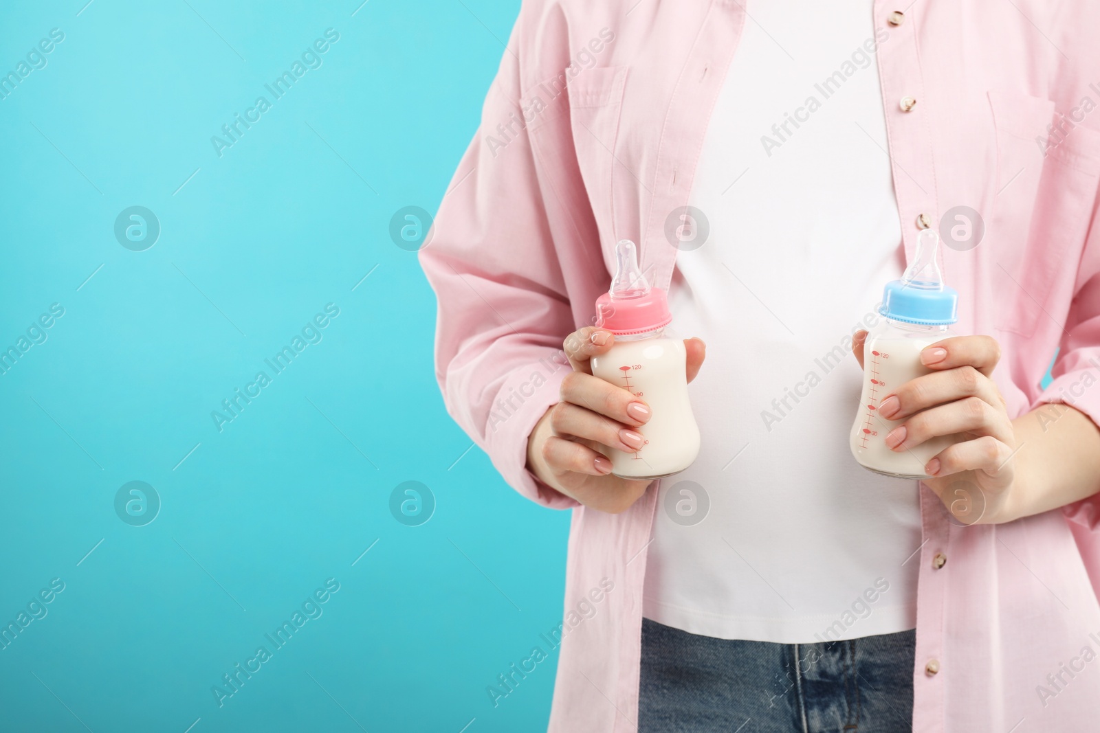 Photo of Expecting twins. Pregnant woman holding two bottles with milk on light blue background, closeup. Space for text