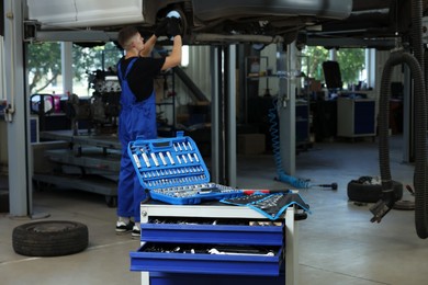 Photo of Auto mechanic fixing lifted car at automobile repair shop, focus on different tools