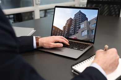 Image of Man looking for house on real estate market website at table, closeup