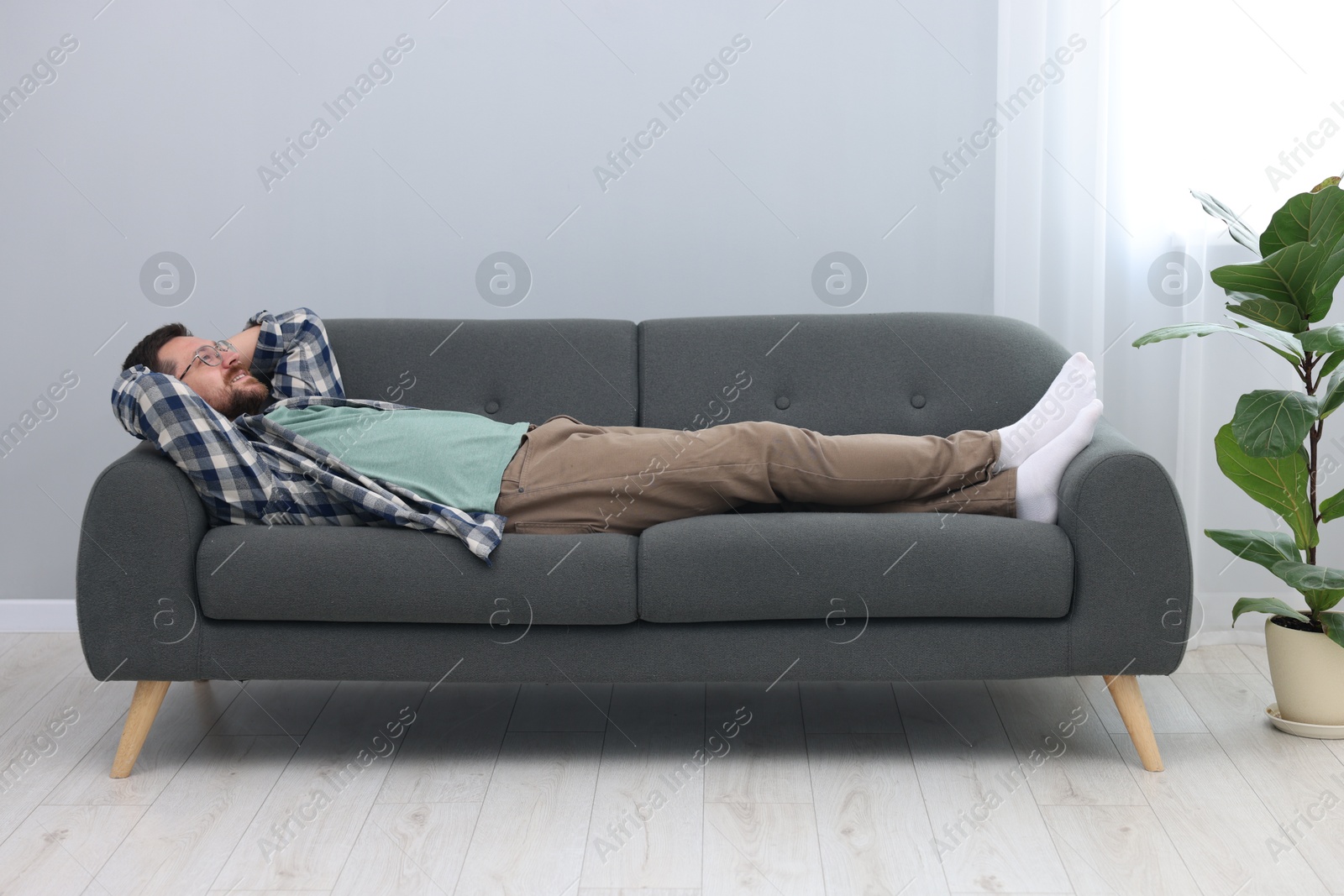 Photo of Smiling man with hands behind his head relaxing on sofa at home