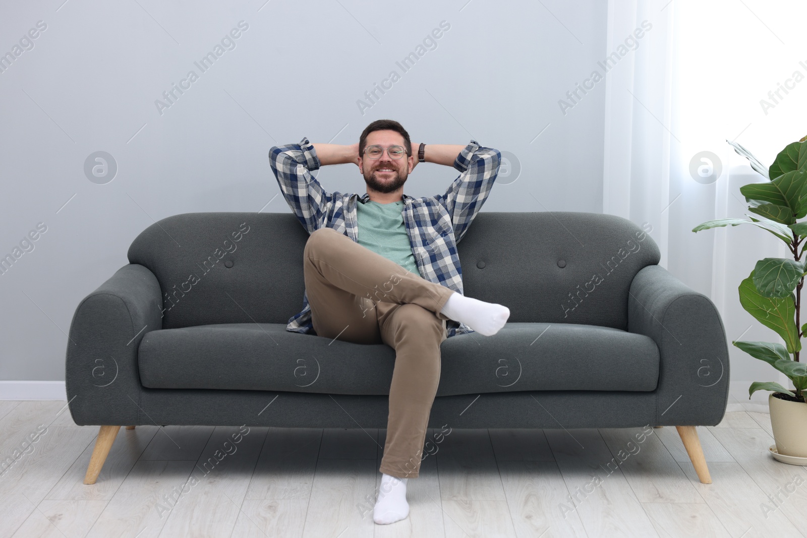 Photo of Smiling man with hands behind his head relaxing on sofa at home