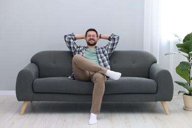 Smiling man with hands behind his head relaxing on sofa at home