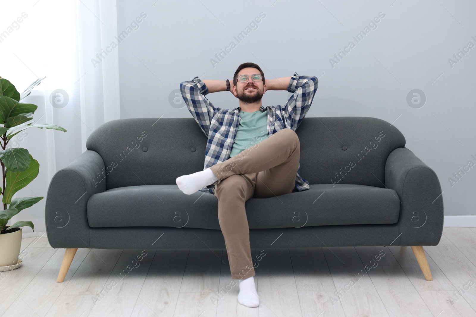 Photo of Smiling man with hands behind his head relaxing on sofa at home