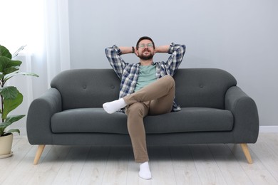 Smiling man with hands behind his head relaxing on sofa at home