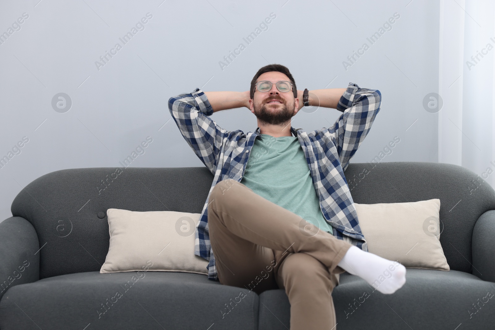 Photo of Smiling man with hands behind his head relaxing on sofa at home