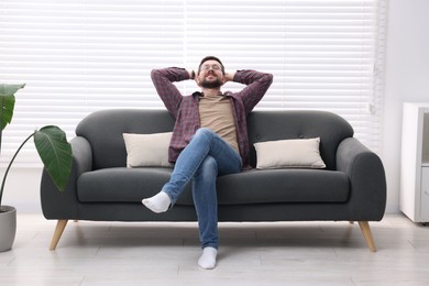 Smiling man with hands behind his head relaxing on sofa at home