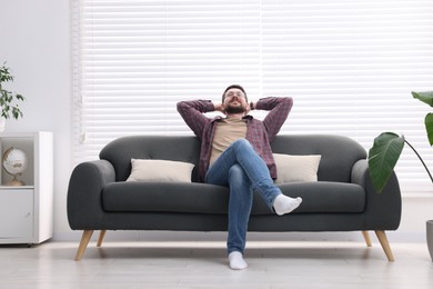 Smiling man with hands behind his head relaxing on sofa at home