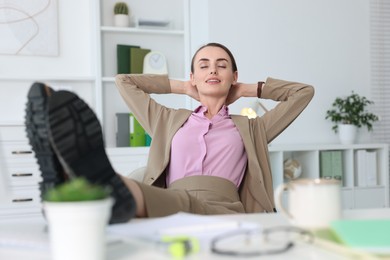 Photo of Smiling businesswoman holding legs on table in office. Break time