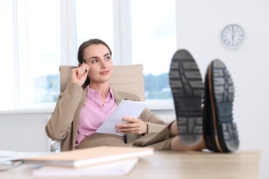 Photo of Beautiful businesswoman working and holding legs at table in office